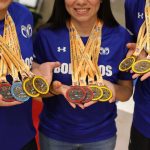 Grupo de atletas sorri e exibe medalhas de ouro, prata e bronze.