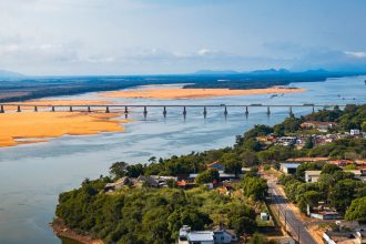 Vista aérea de ponte sobre um rio em Boa Vista, cercada por áreas verdes sob céu claro.