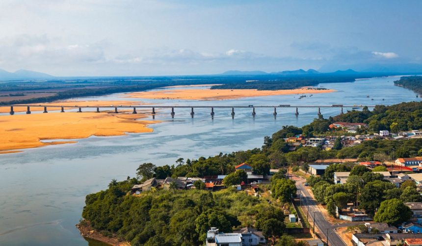 Vista aérea de ponte sobre um rio em Boa Vista, cercada por áreas verdes sob céu claro.
