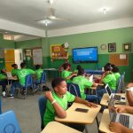 Estudantes participam de uma aula em sala, utilizando laptops e acompanhando a atividade.