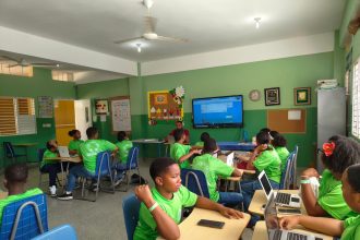 Estudantes participam de uma aula em sala, utilizando laptops e acompanhando a atividade.