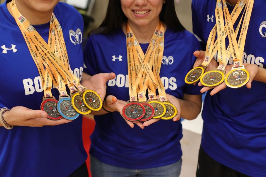 Grupo de atletas sorri e exibe medalhas de ouro, prata e bronze.