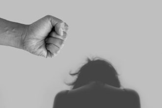 Imagem conceitual em tons de cinza sobre violência contra a mulher, com representação de ameaça, agressão e desigualdade de gênero.