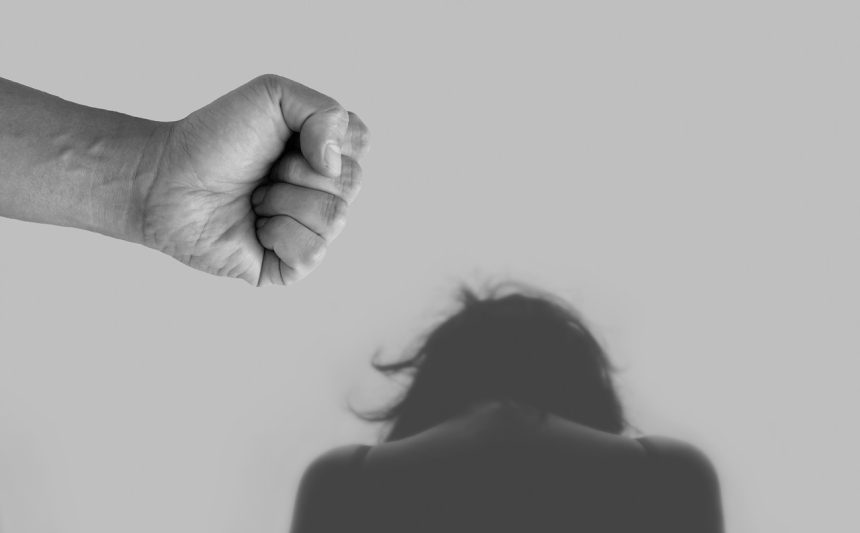 Imagem conceitual em tons de cinza sobre violência contra a mulher, com representação de ameaça, agressão e desigualdade de gênero.